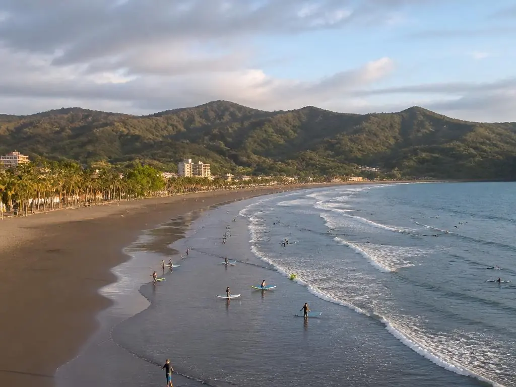 Beginner surfers along the long grey-sand beach at Jacó